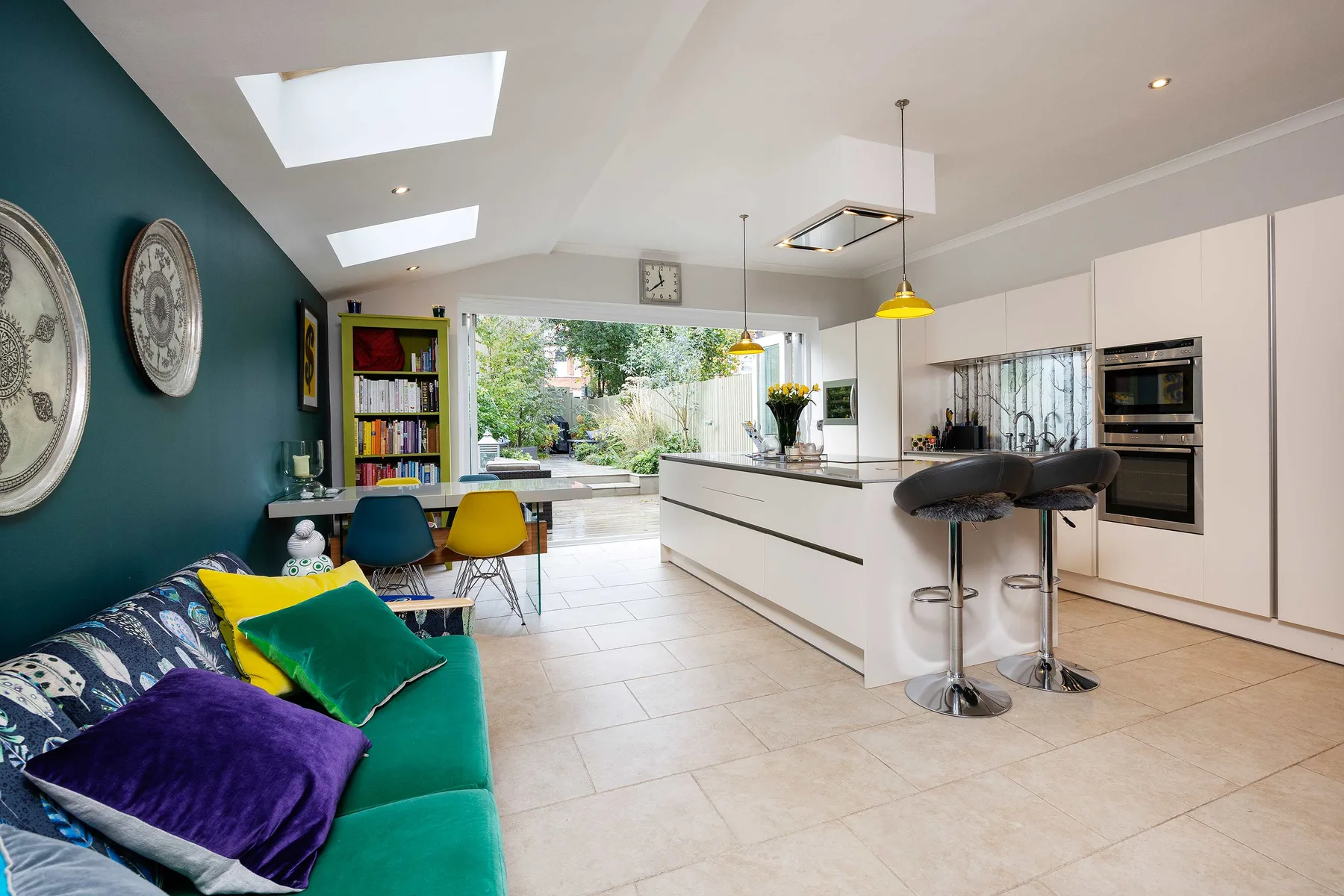 Una luminosa cocina y sala de estar de concepto abierto, con una isla blanca larga y asientos coloridos.
