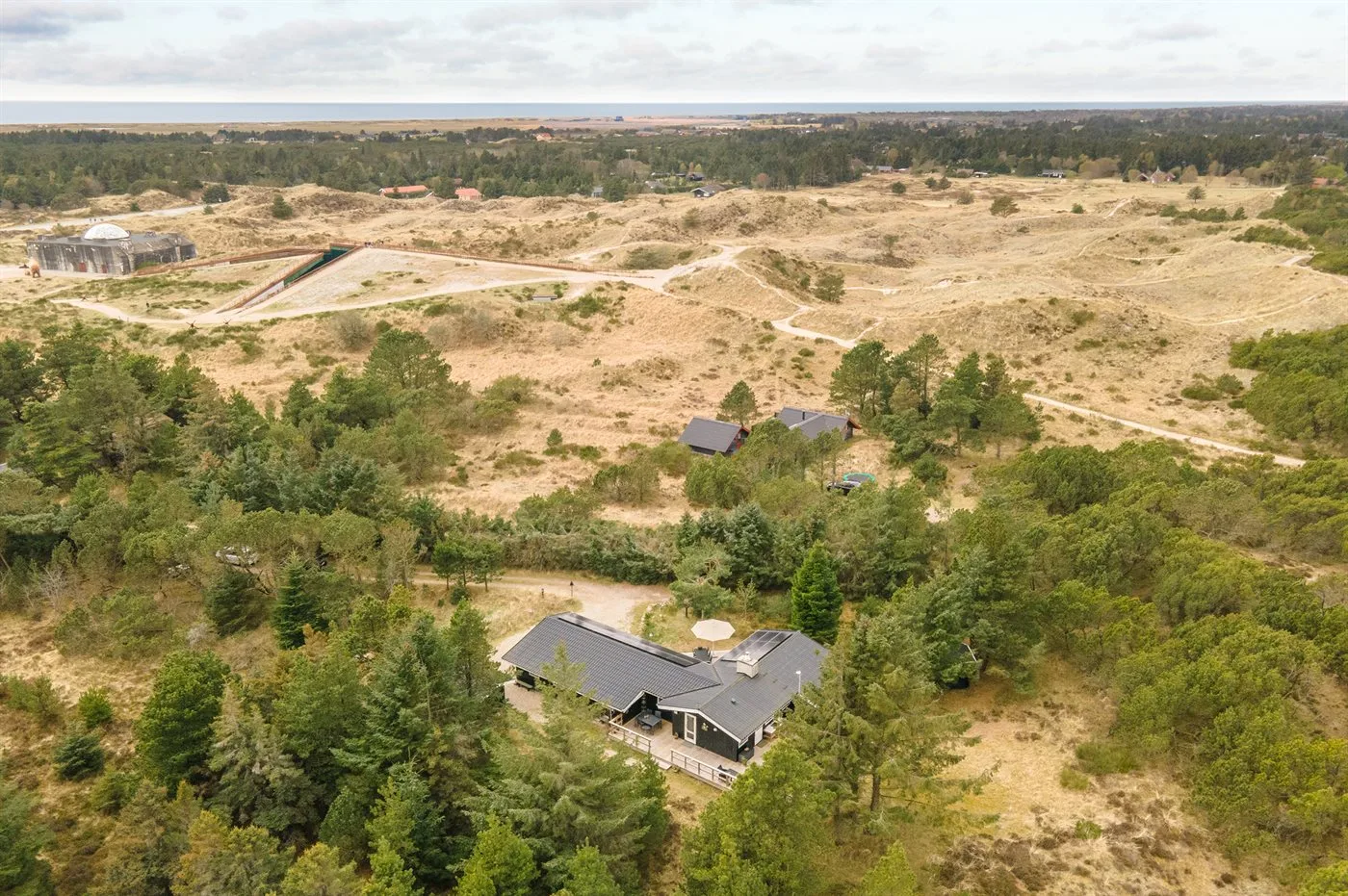 Aerial view of a house surrounded by trees and open, sandy terrain.