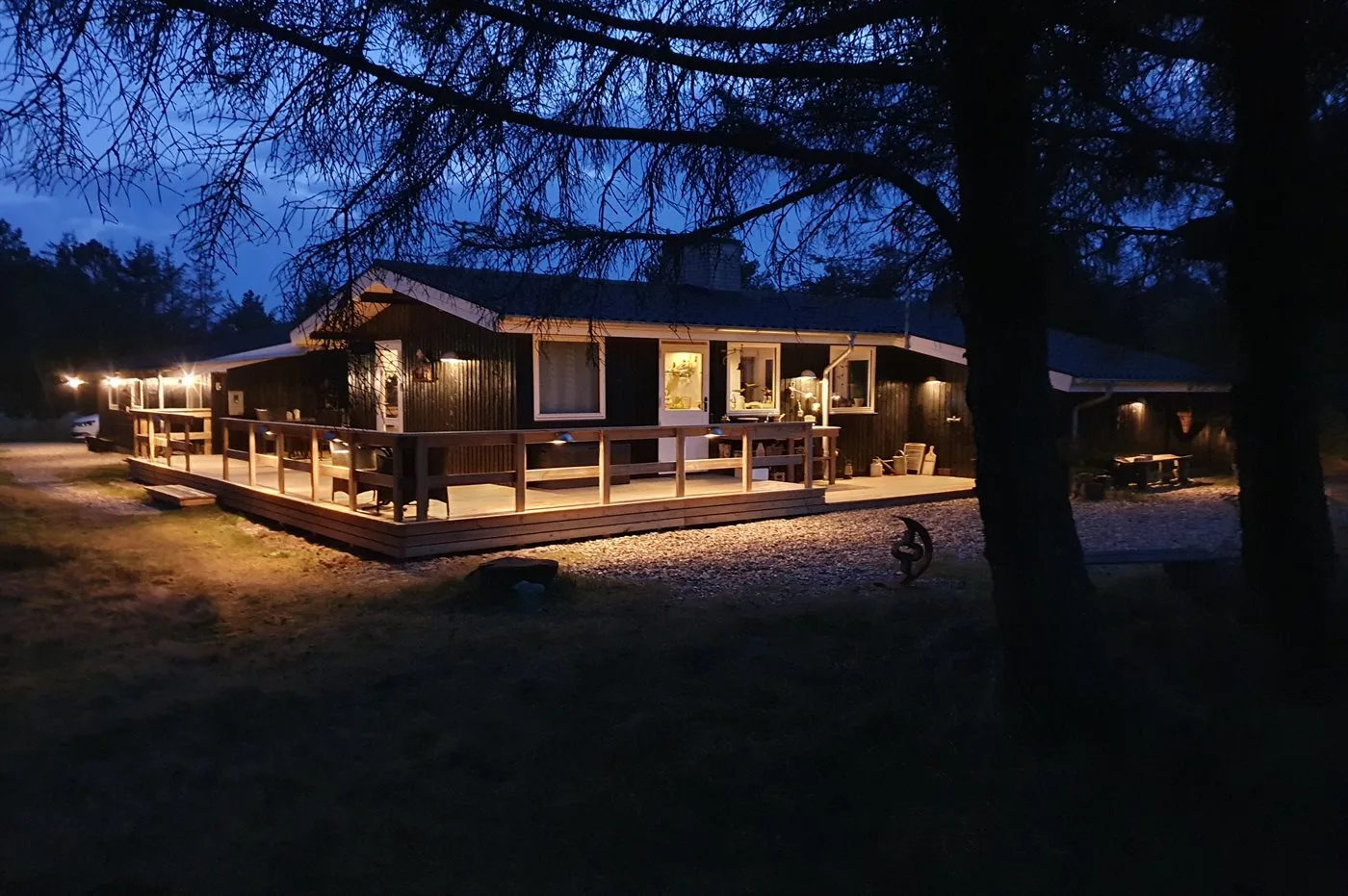 A wooden building with a warmly lit wraparound deck at dusk.
