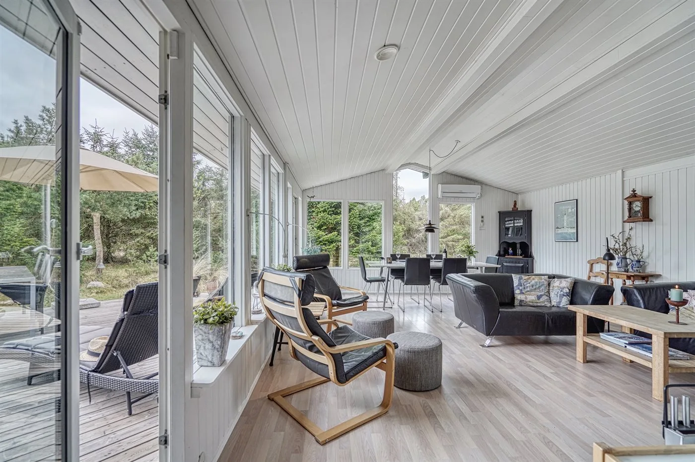A bright living room with seating and large windows overlooking greenery.