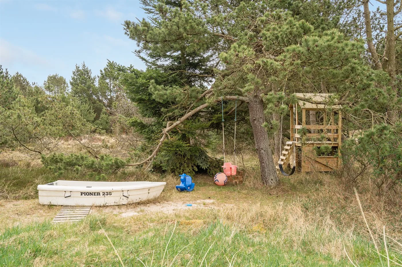 A small boat rests in a grassy clearing beside a wooden tree platform.