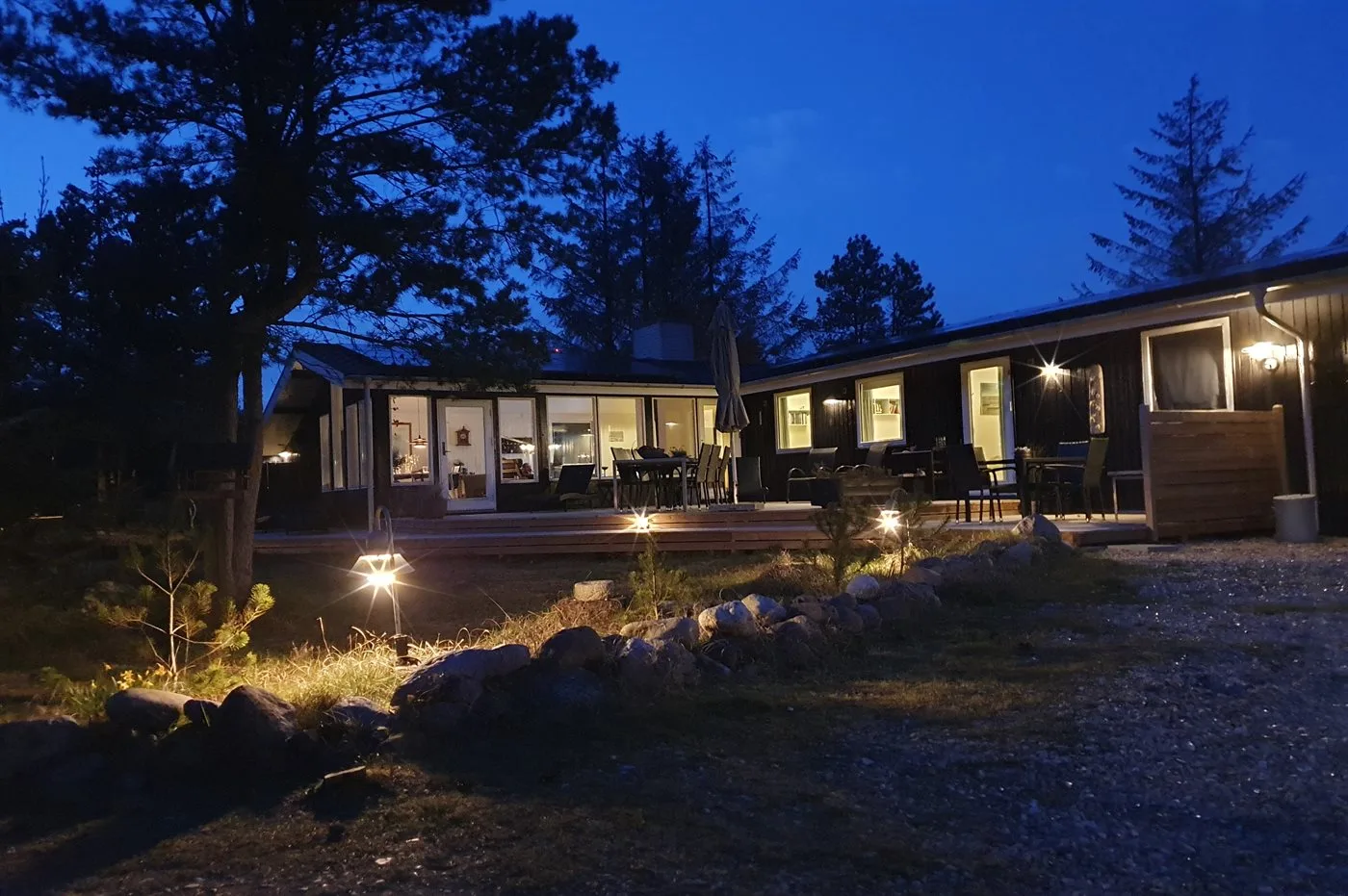 A modern house glows at dusk, with large windows and outdoor seating.
