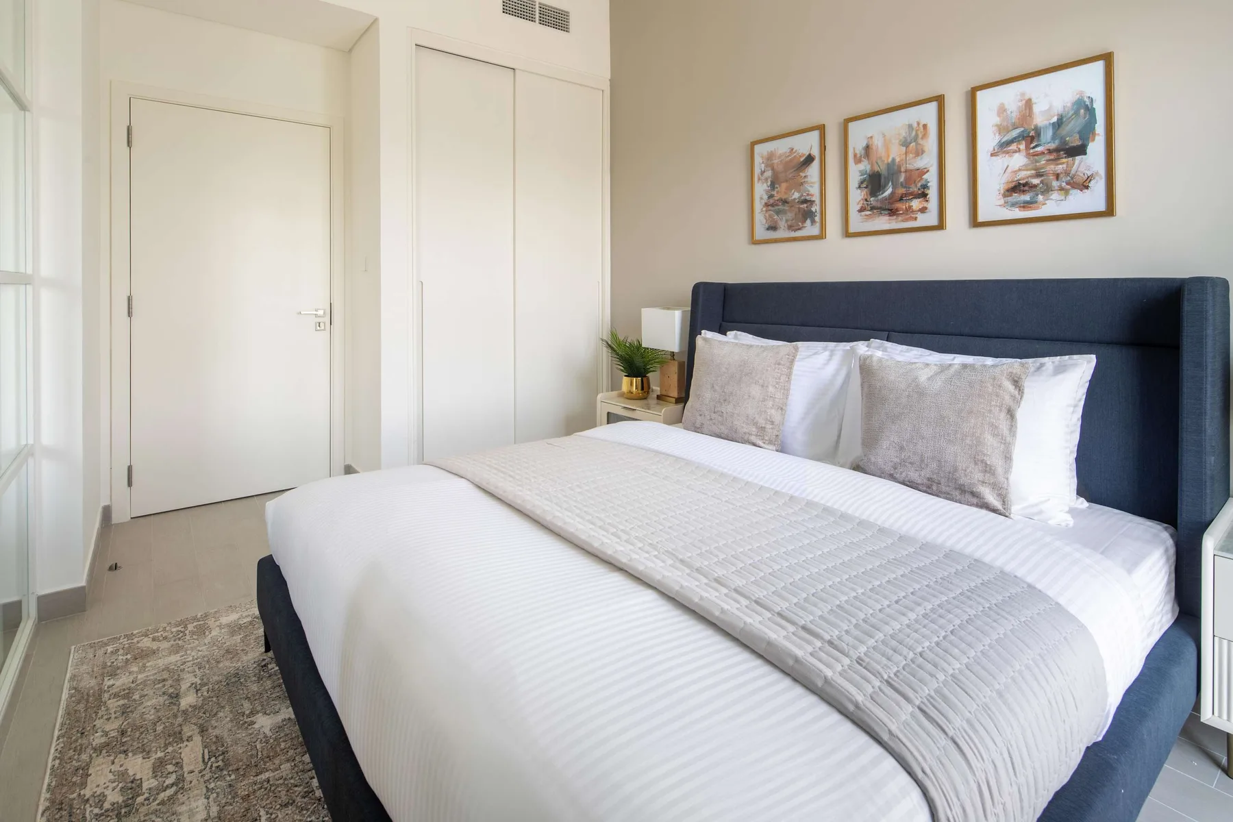 Un dormitorio luminoso con una cama bien hecha bajo tres cuadros enmarcados.