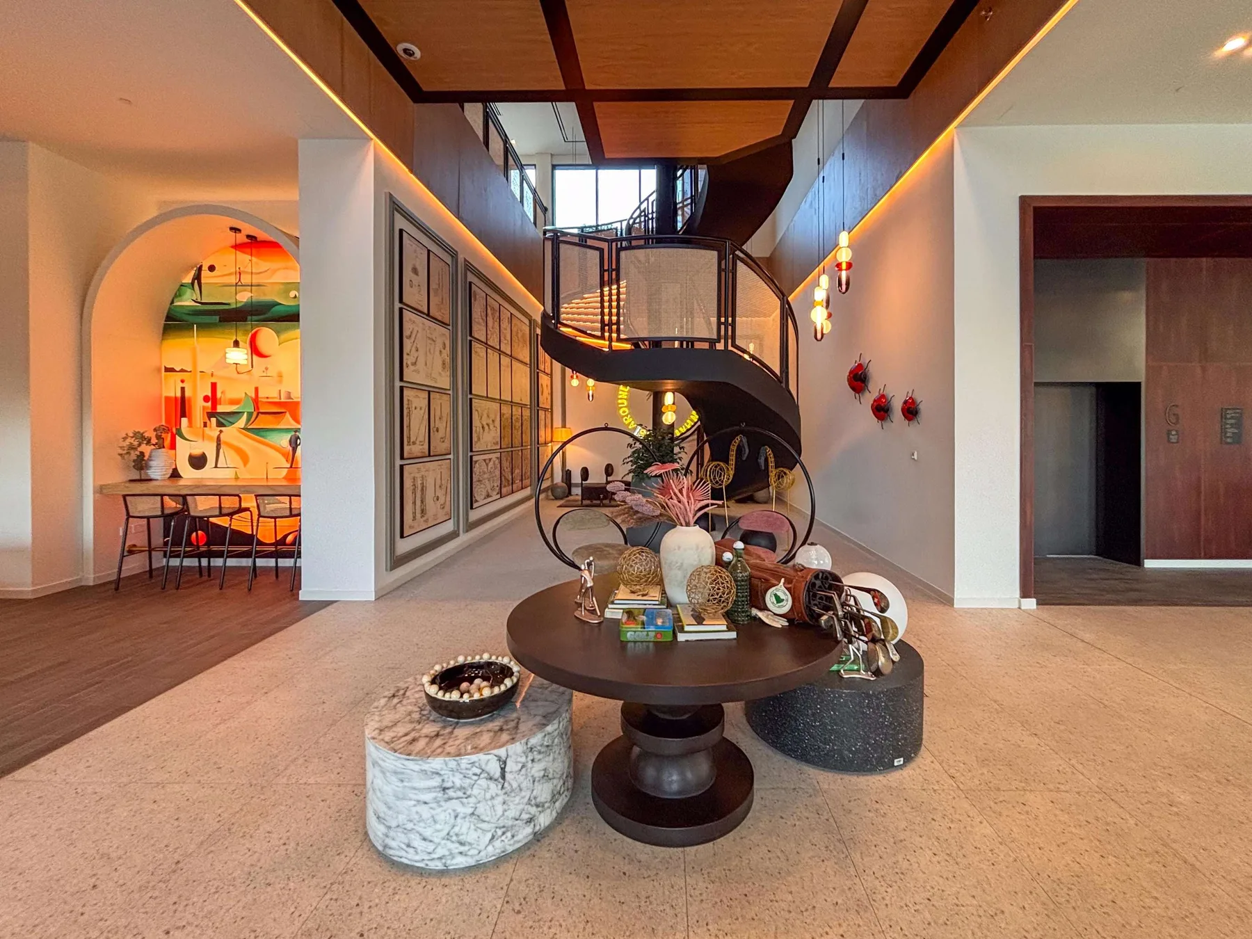 Un interior amplio presenta una escalera curva y una mesa redonda con objetos decorativos.