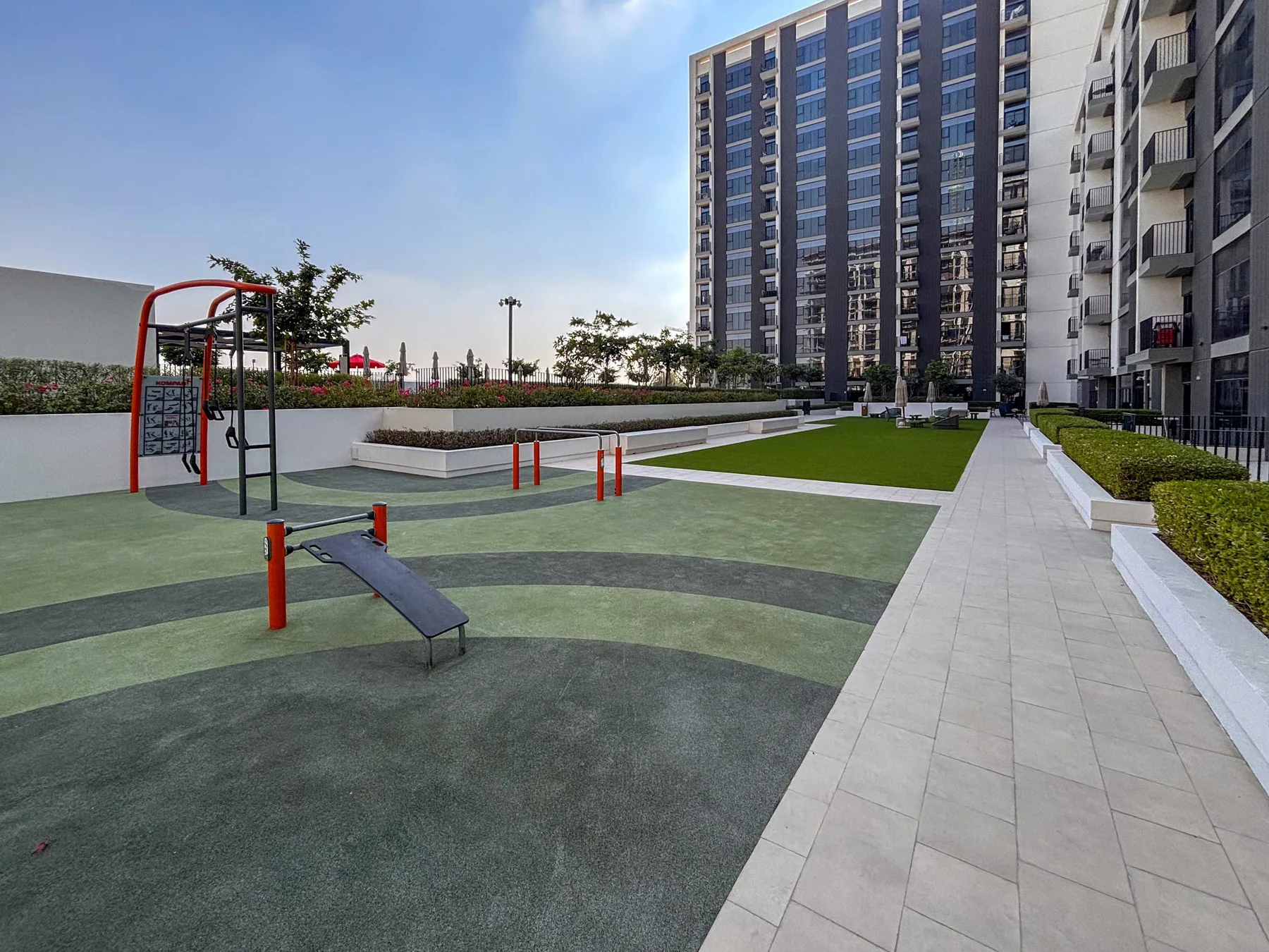 Una zona de ejercicio al aire libre junto a un sendero pavimentado y edificios altos.
