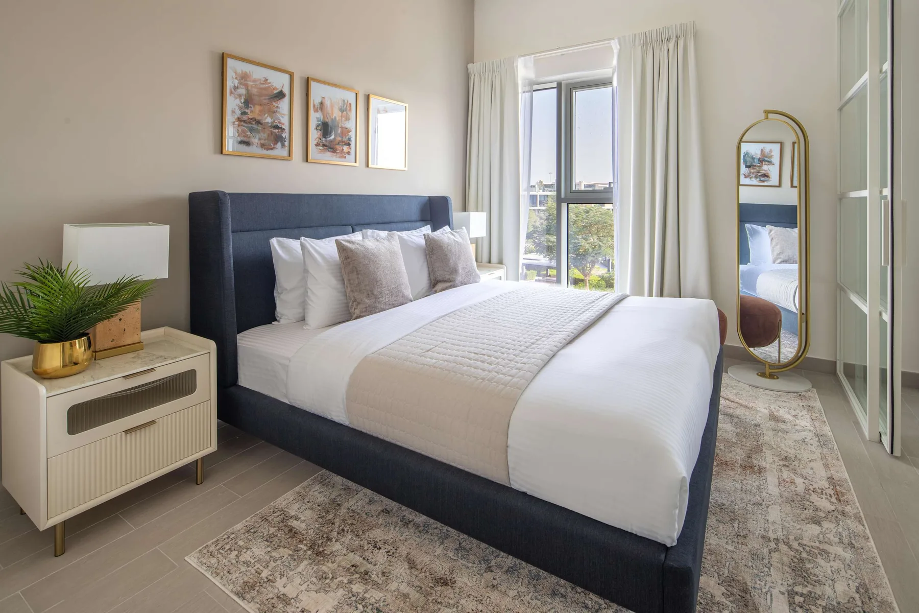 Dormitorio con una cama bien tendida, una mesita de noche y ventanas altas.