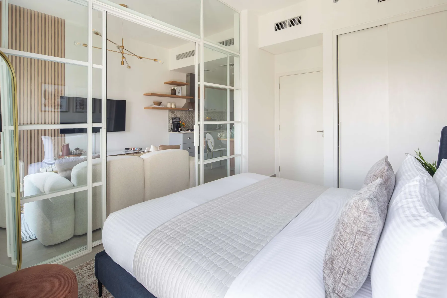 Un dormitorio luminoso con una cama tendida y mamparas de vidrio.
