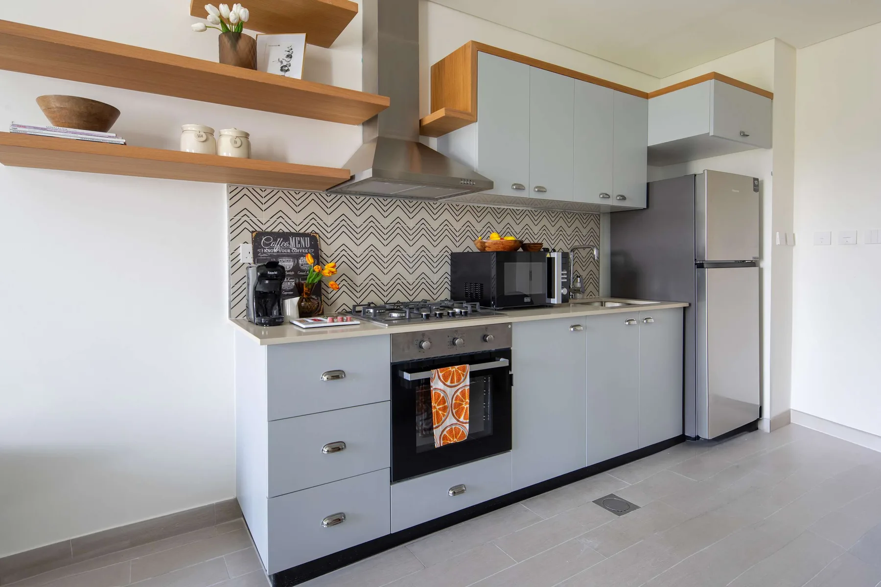 Una cocina moderna con gabinetes grises, un salpicadero estampado y electrodomésticos sobre la encimera.