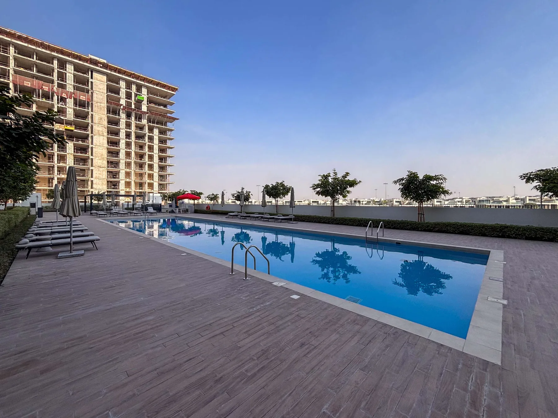 Una piscina al aire libre junto a un edificio, con asientos en la terraza.
