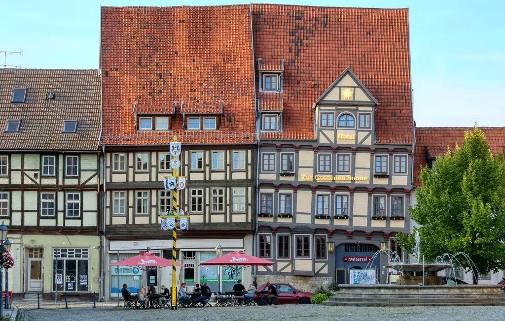 A row of half-timbered town buildings with red tiled roofs and a small outdoor café.
