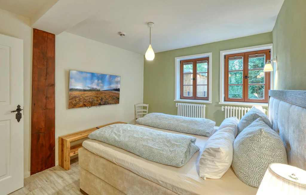 A bedroom with two beds, a wall-mounted landscape picture, and windows.