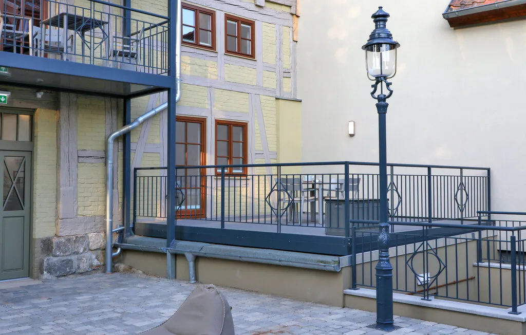 A paved courtyard with a metal-railed balcony and a tall lamp.