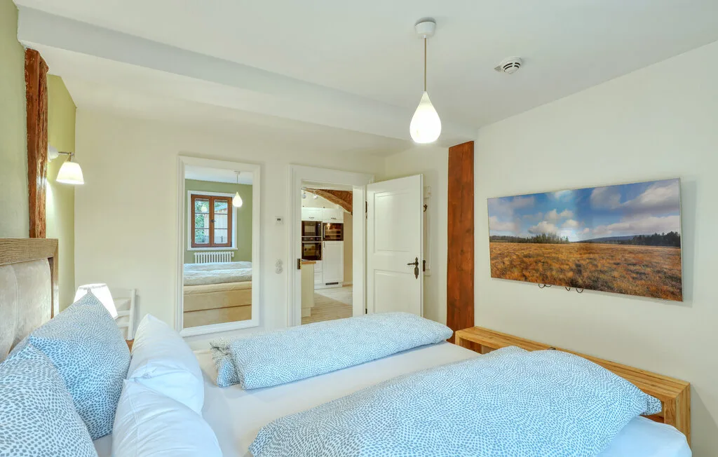 A bright bedroom with blue bedding and a landscape picture on the wall.
