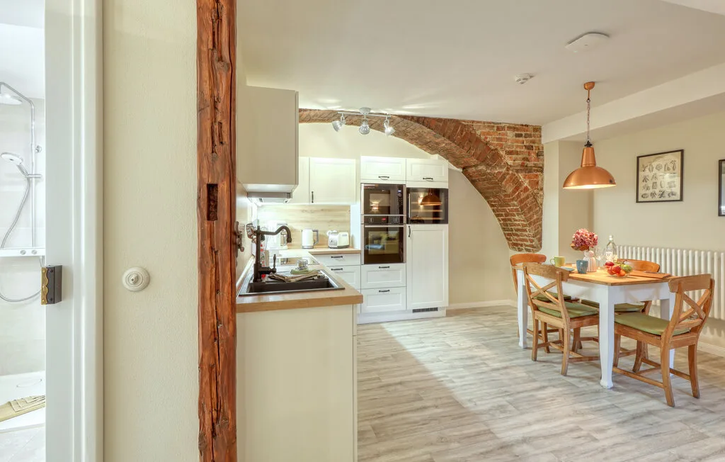 Una luminosa cocina y comedor con armarios blancos y una mesa de madera.