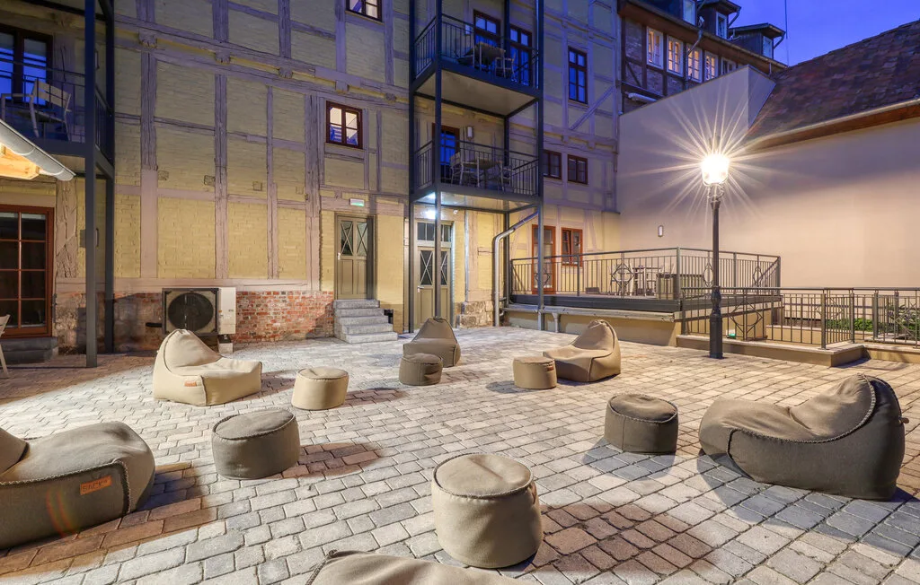 A paved courtyard with low cushioned seating and a lit outdoor lamp.