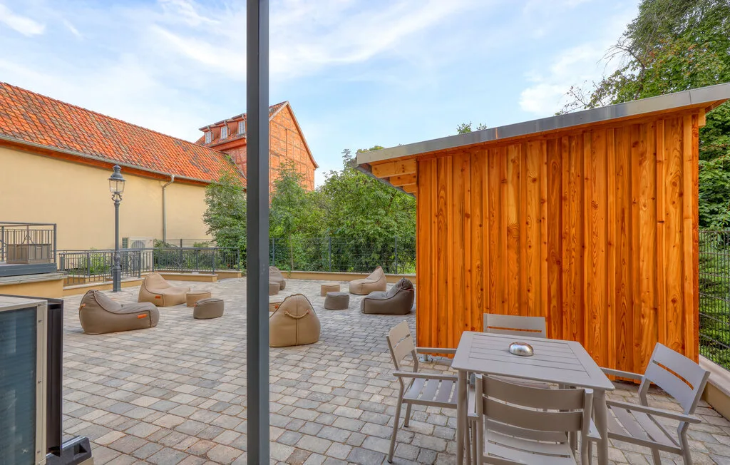 An outdoor patio has seating and a dining table beside a wooden structure.