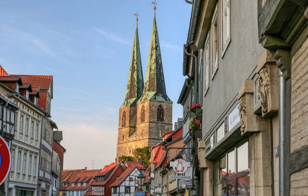 A historic town street with red-roofed buildings and twin church spires.
