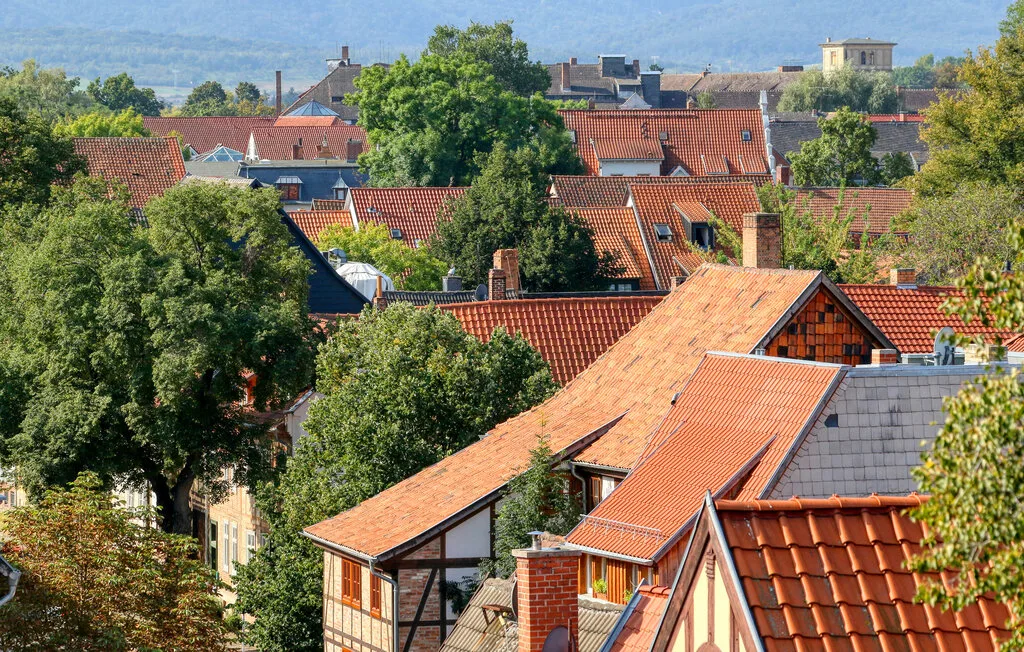 A cluster of red-tiled rooftops sits among leafy trees, with hills in the distance.