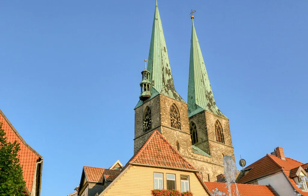 A historic church with twin green spires rises above red-tiled rooftops.