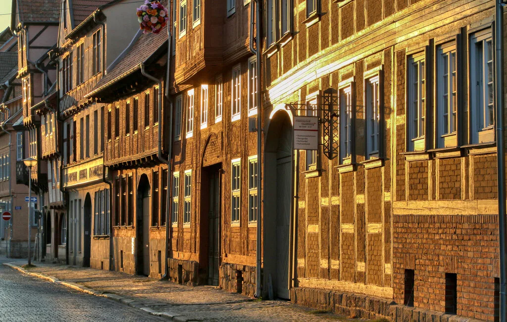 A sunlit cobblestone street runs beside a row of historic-looking buildings.