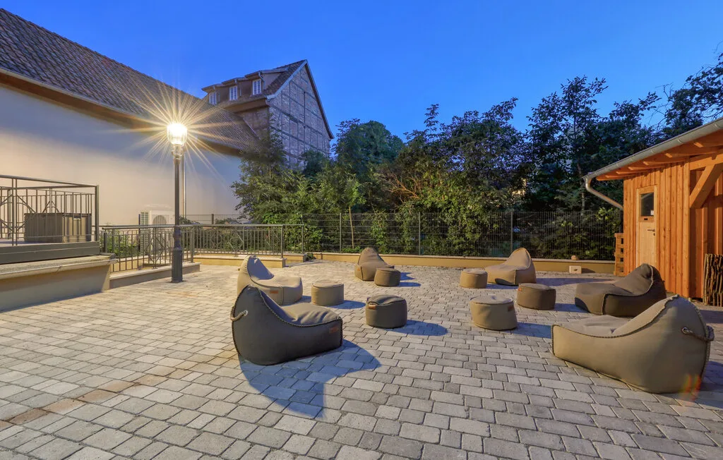A paved outdoor patio has scattered seating beside a wooden structure.