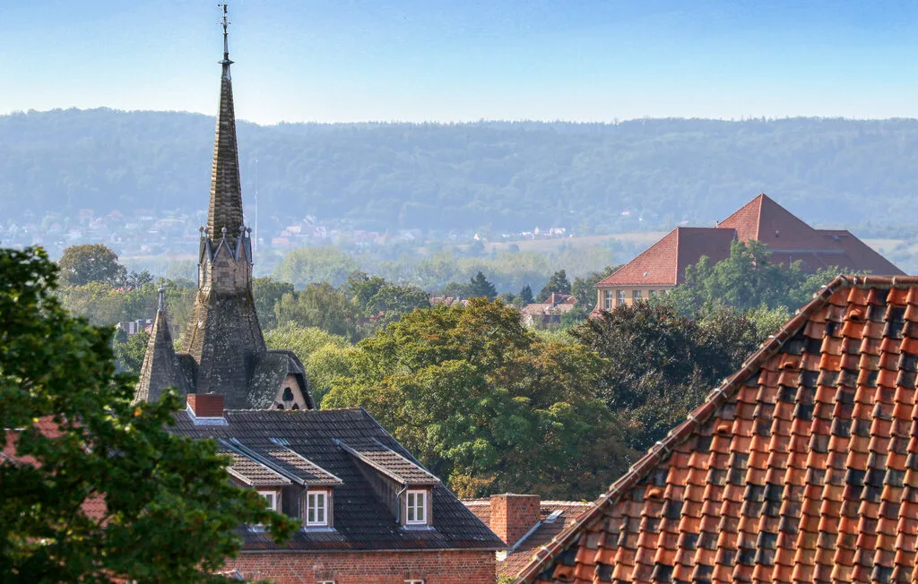 A church steeple rises above rooftops and leafy trees, with hills in the distance.