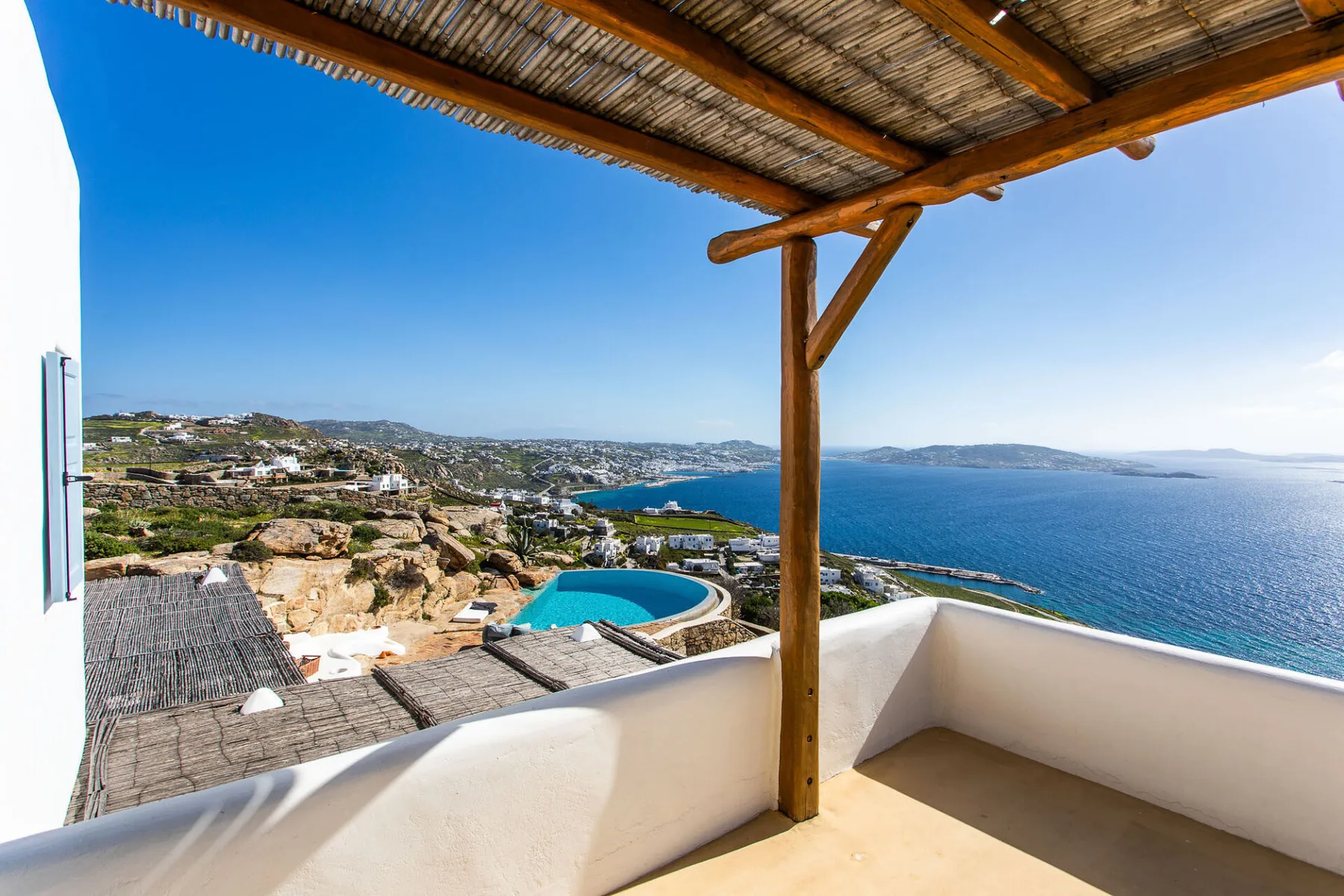 A covered terrace overlooks a swimming pool, coastal hillside, and sea.