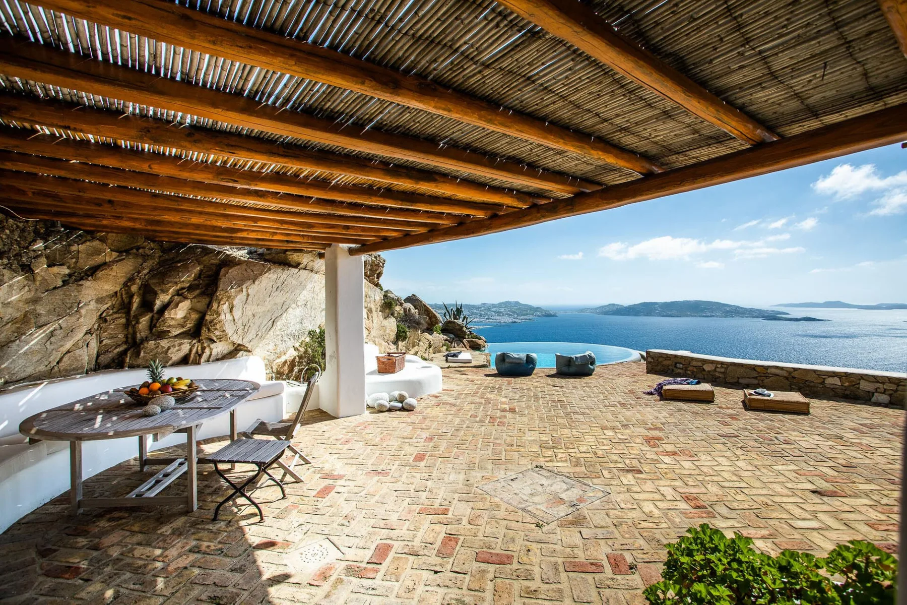 A covered outdoor terrace overlooks the sea, with a dining table and seating.