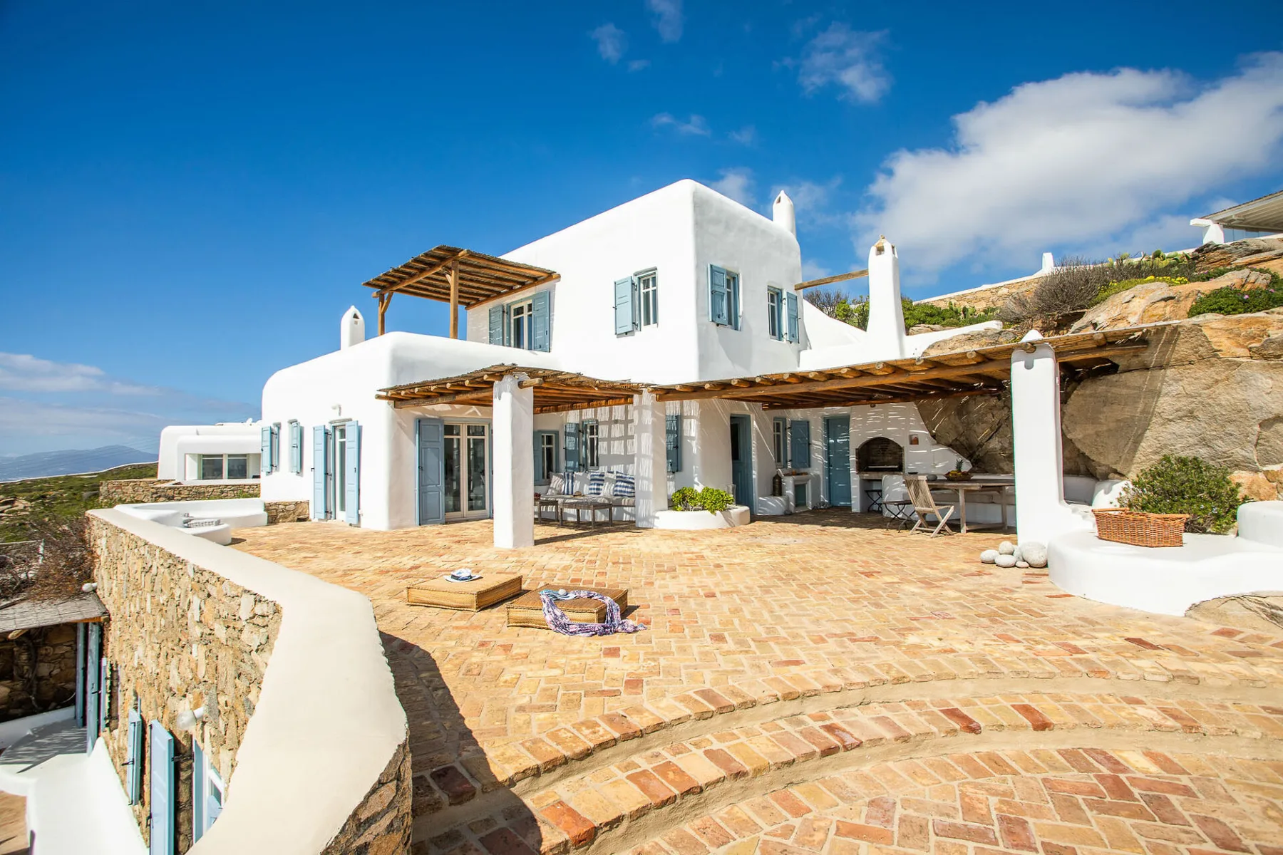 A white villa opens onto a broad brick-paved terrace with outdoor seating.