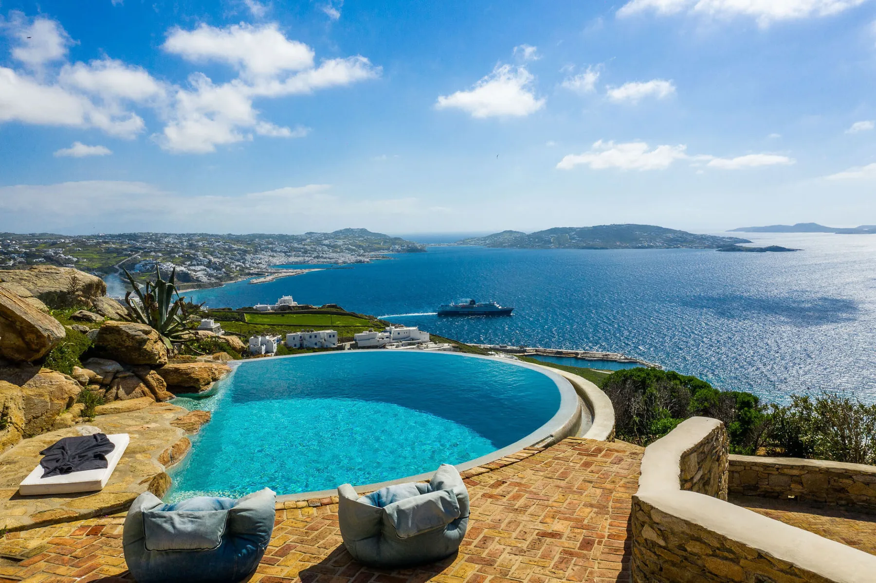 A curved swimming pool overlooks a blue sea and distant coastline.