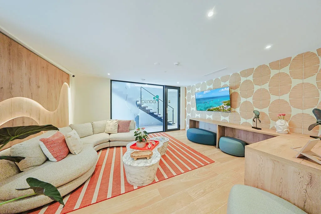 A Modern reception/lounge space, a plush curved sofa, natural light pouring through the wall of windows, a comfortable space to plan your island adventures or to relax after a day of exlploring.