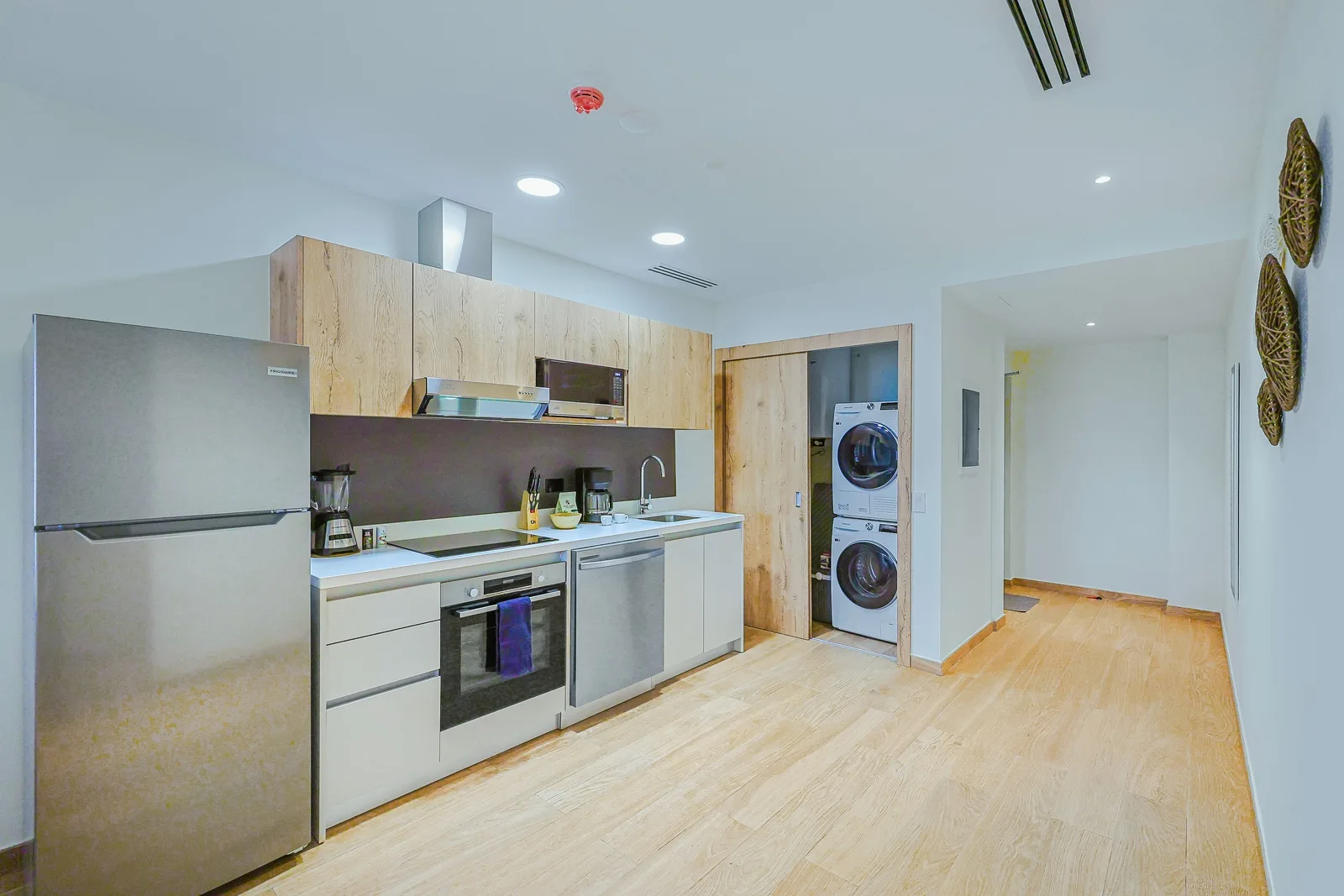 Your fully equipped kitchen features sleek modern appliances, natural wood cabinetry, and a washer-dryer combo tucked neatly behind wooden doors—everything you need for a comfortable stay.