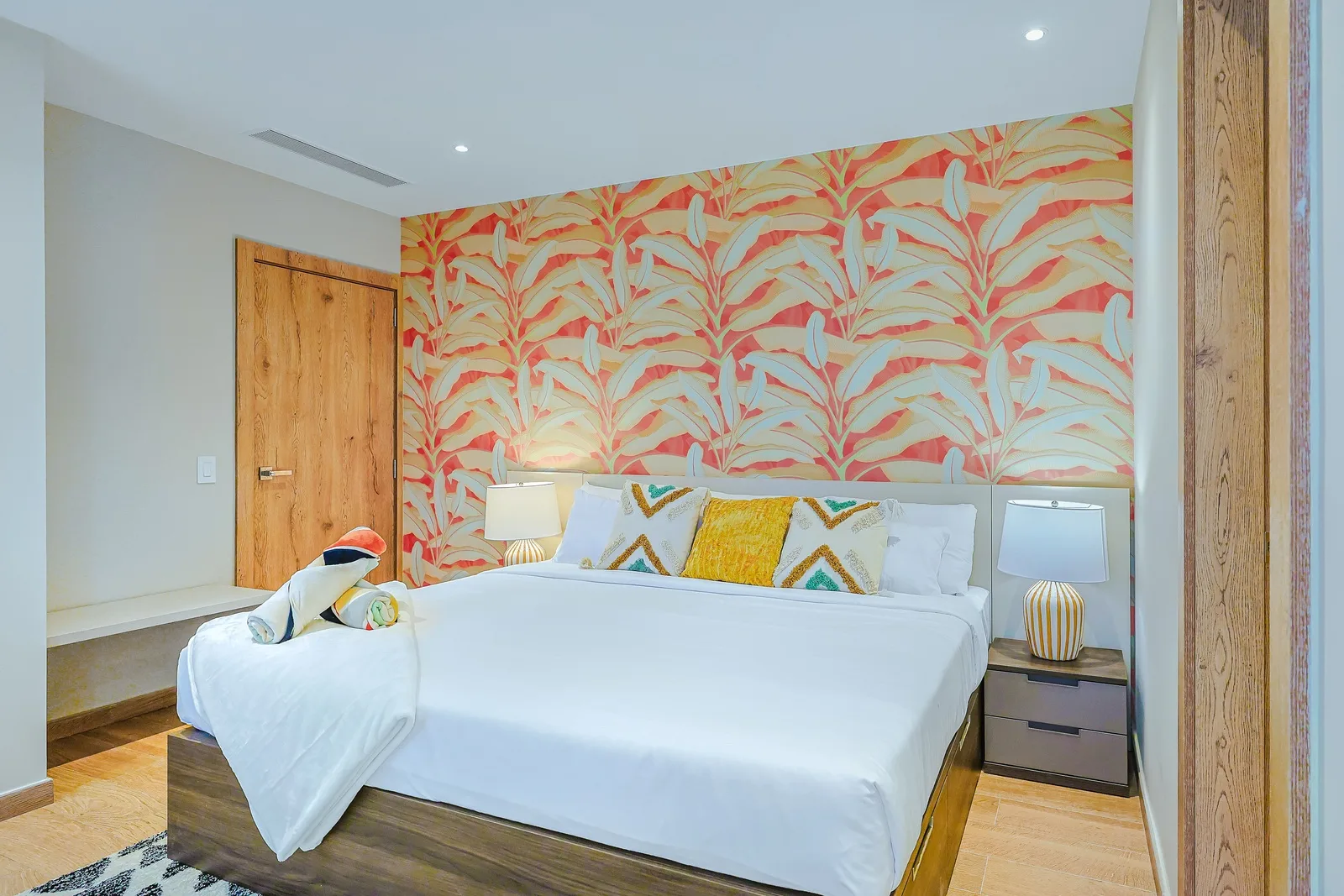 Sink into this cozy retreat where vibrant tropical patterns meet crisp white linens. Your peaceful getaway awaits with modern touches and warm natural wood accents throughout.