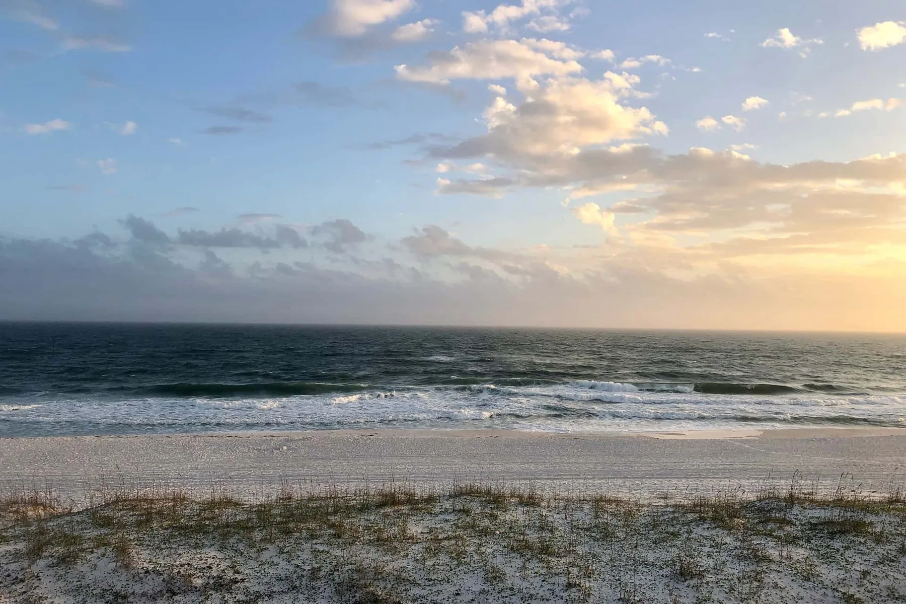 Una playa de arena bordea el océano bajo un cielo nublado al atardecer.