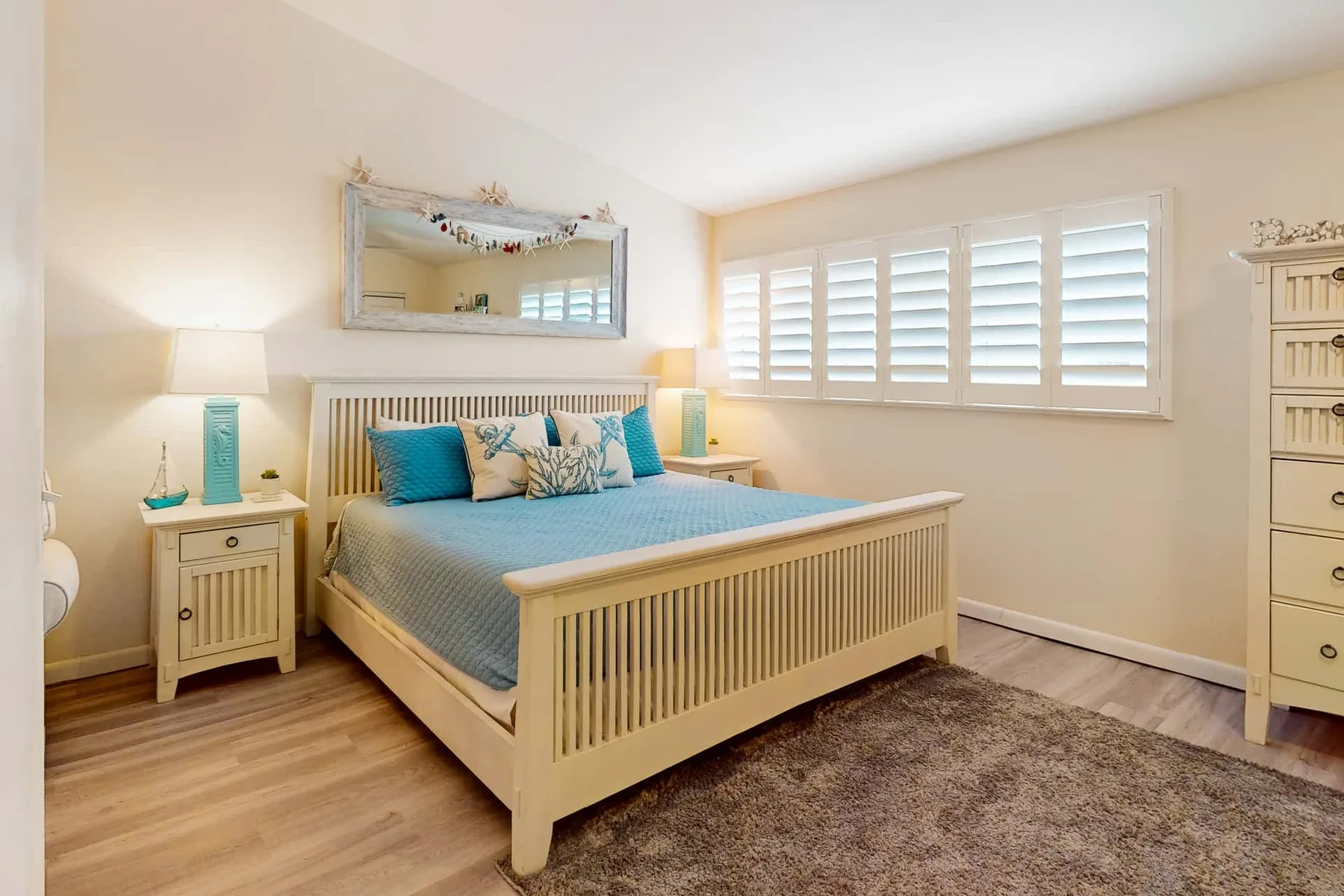 Un dormitorio luminoso con cama, mesillas y ventanas con contraventanas.