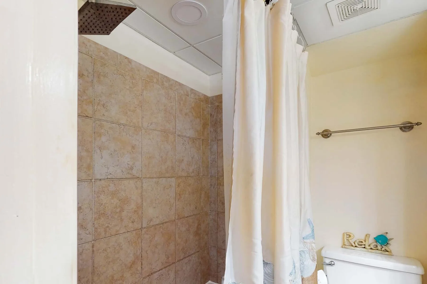 Zona de ducha de un baño con paredes de azulejos y cortina blanca.