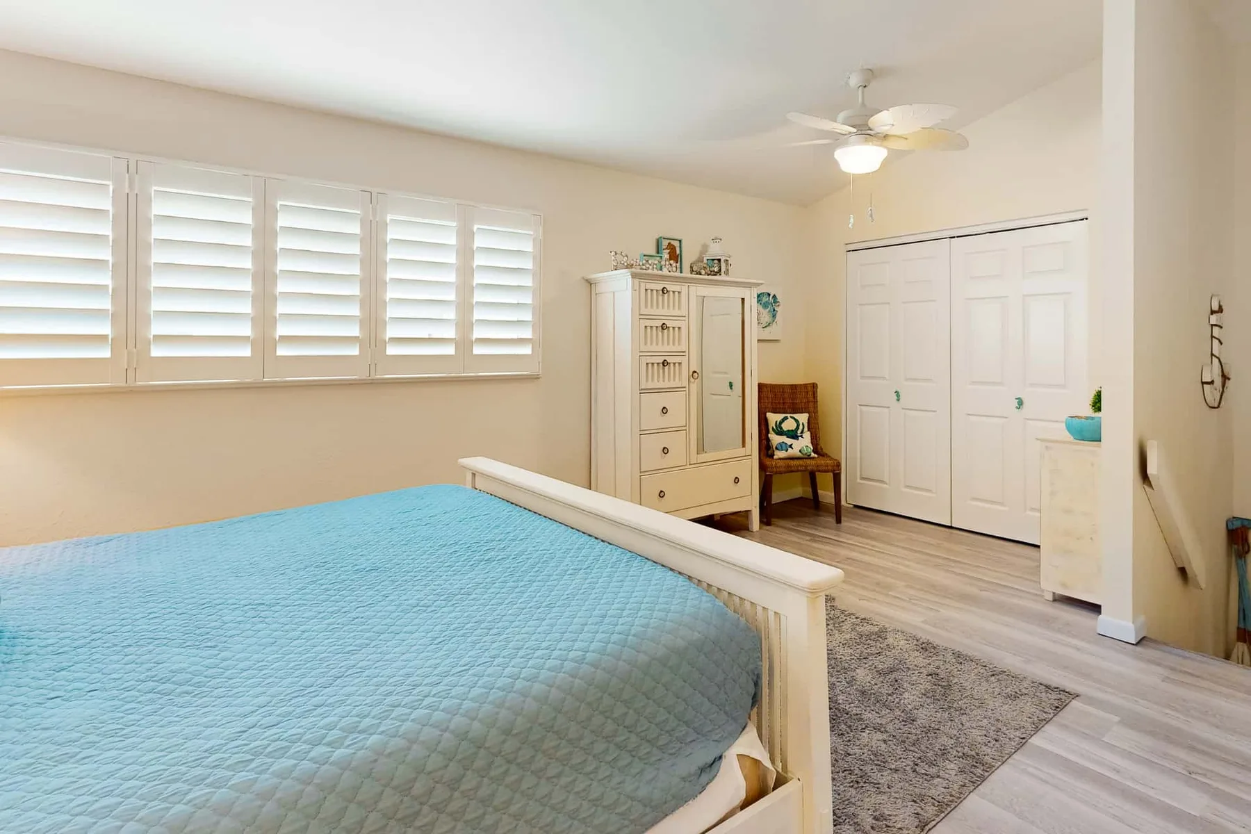 Un dormitorio con una cama, ventanas con contraventanas y una cómoda blanca.