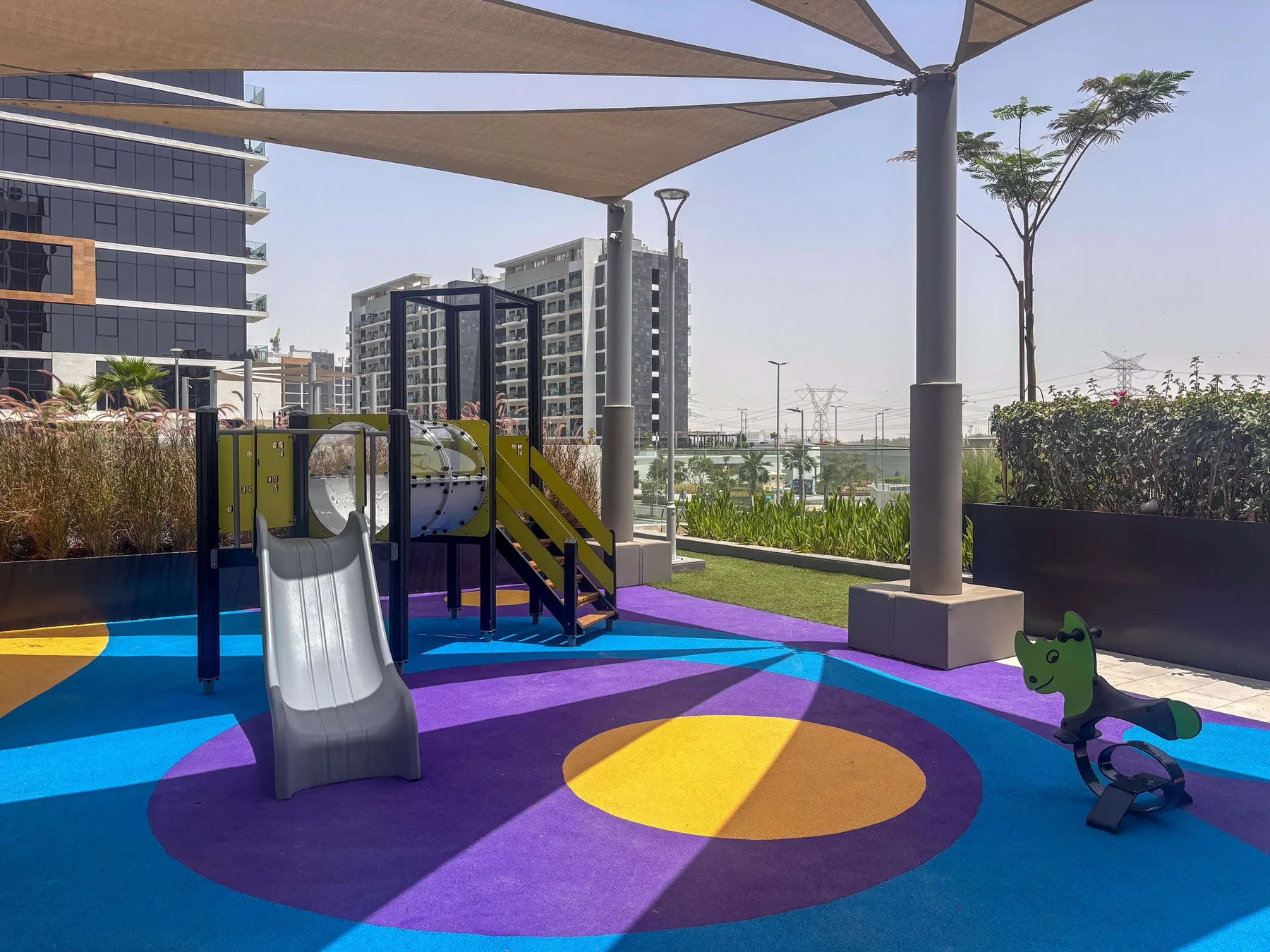 Un parque infantil al aire libre con suelo de colores, un tobogán y juegos para trepar.