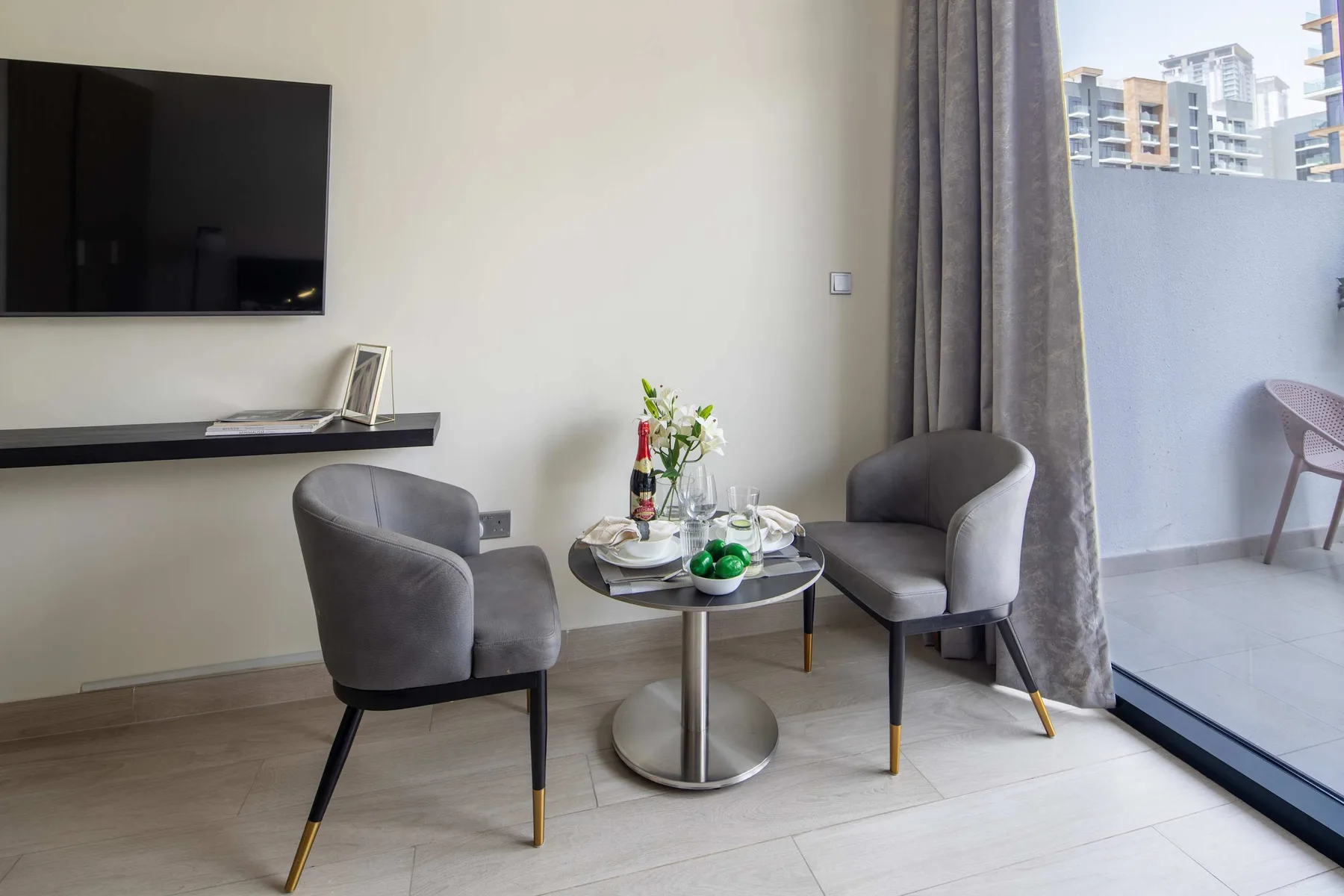 Una zona de estar con dos sillones, una mesa pequeña y un televisor en la pared.
