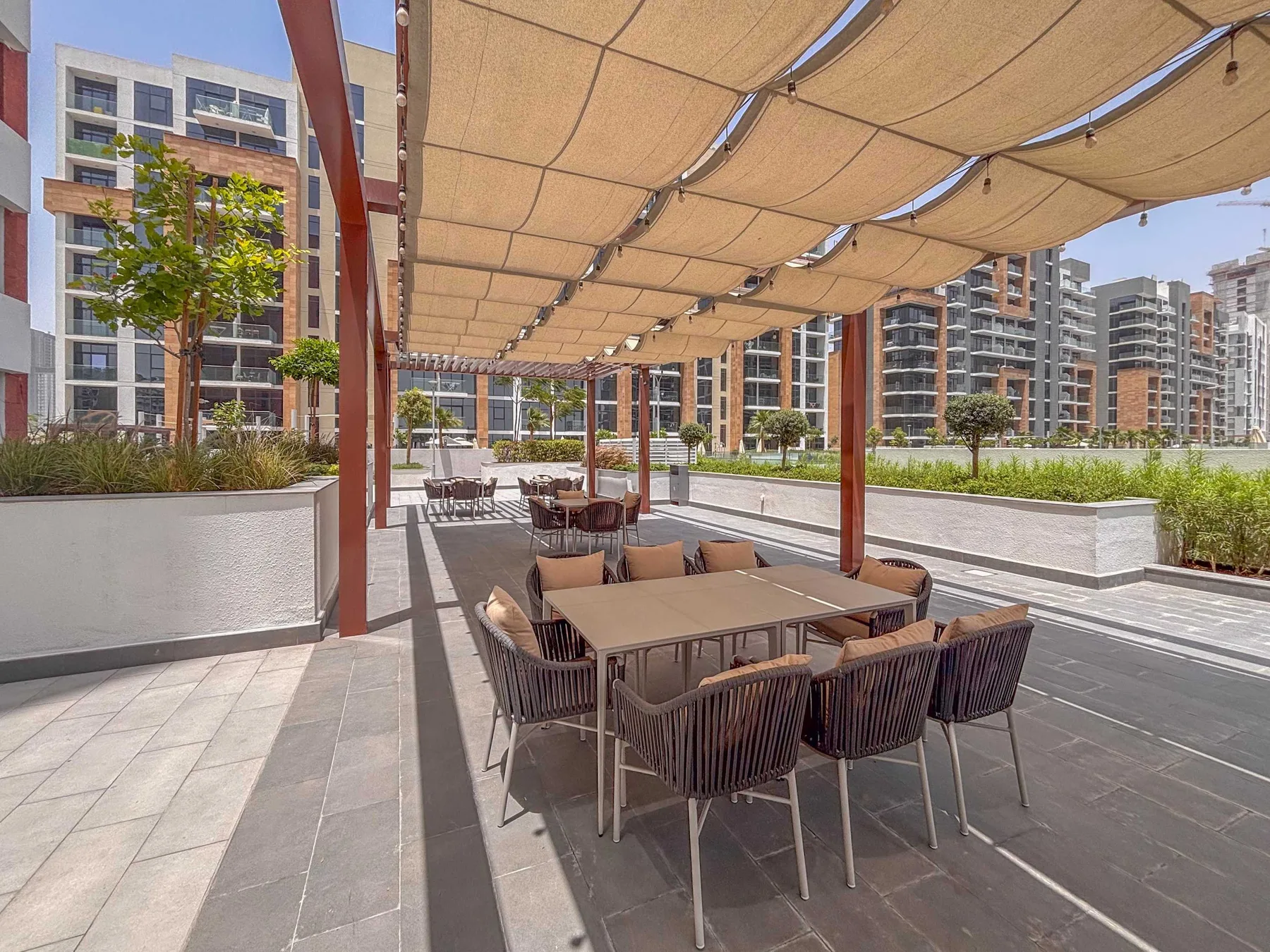 Una zona de comedor al aire libre con mesas y asientos bajo una cubierta de tela.
