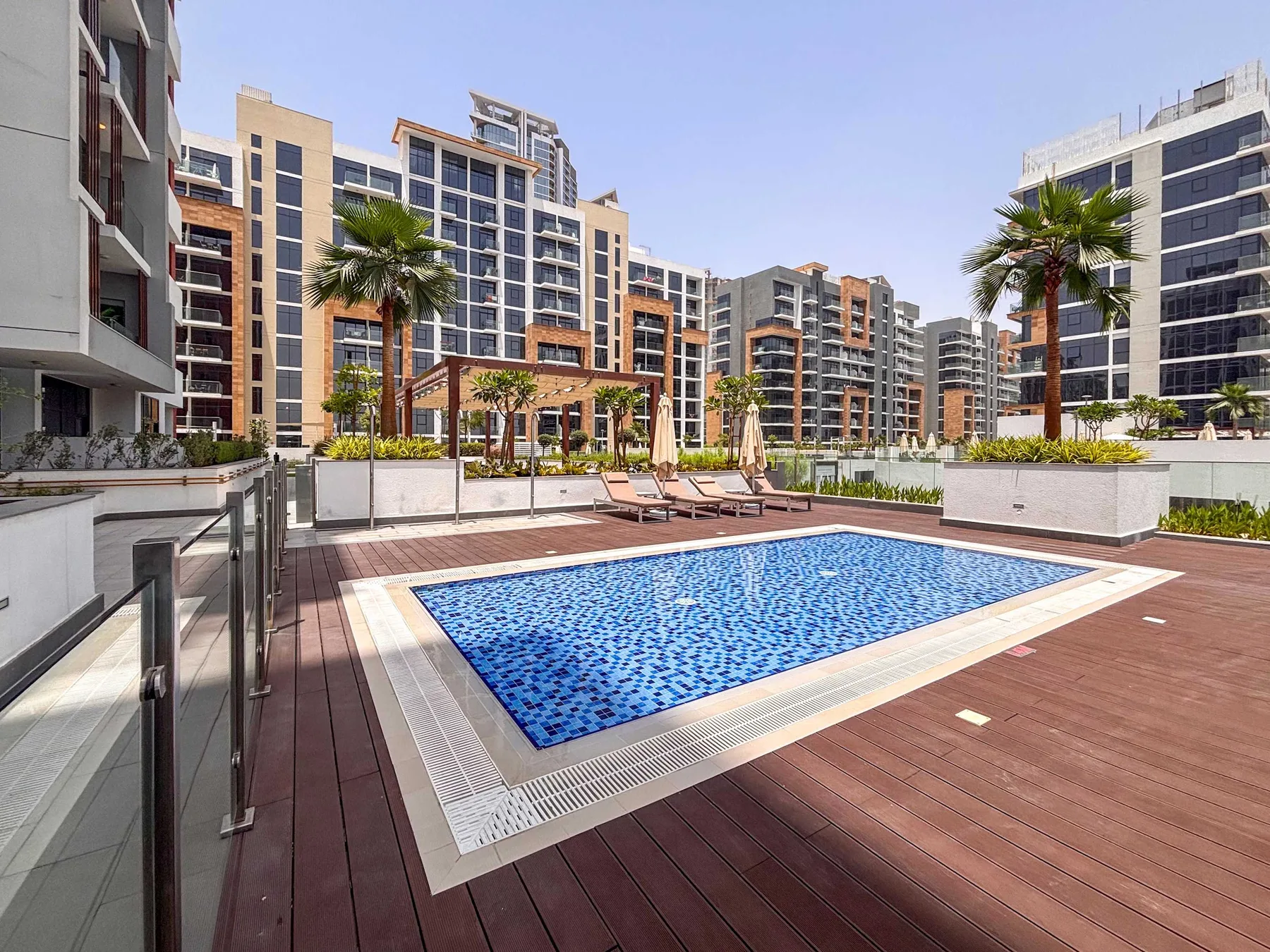Una piscina al aire libre ocupa una terraza de madera entre edificios de apartamentos modernos.