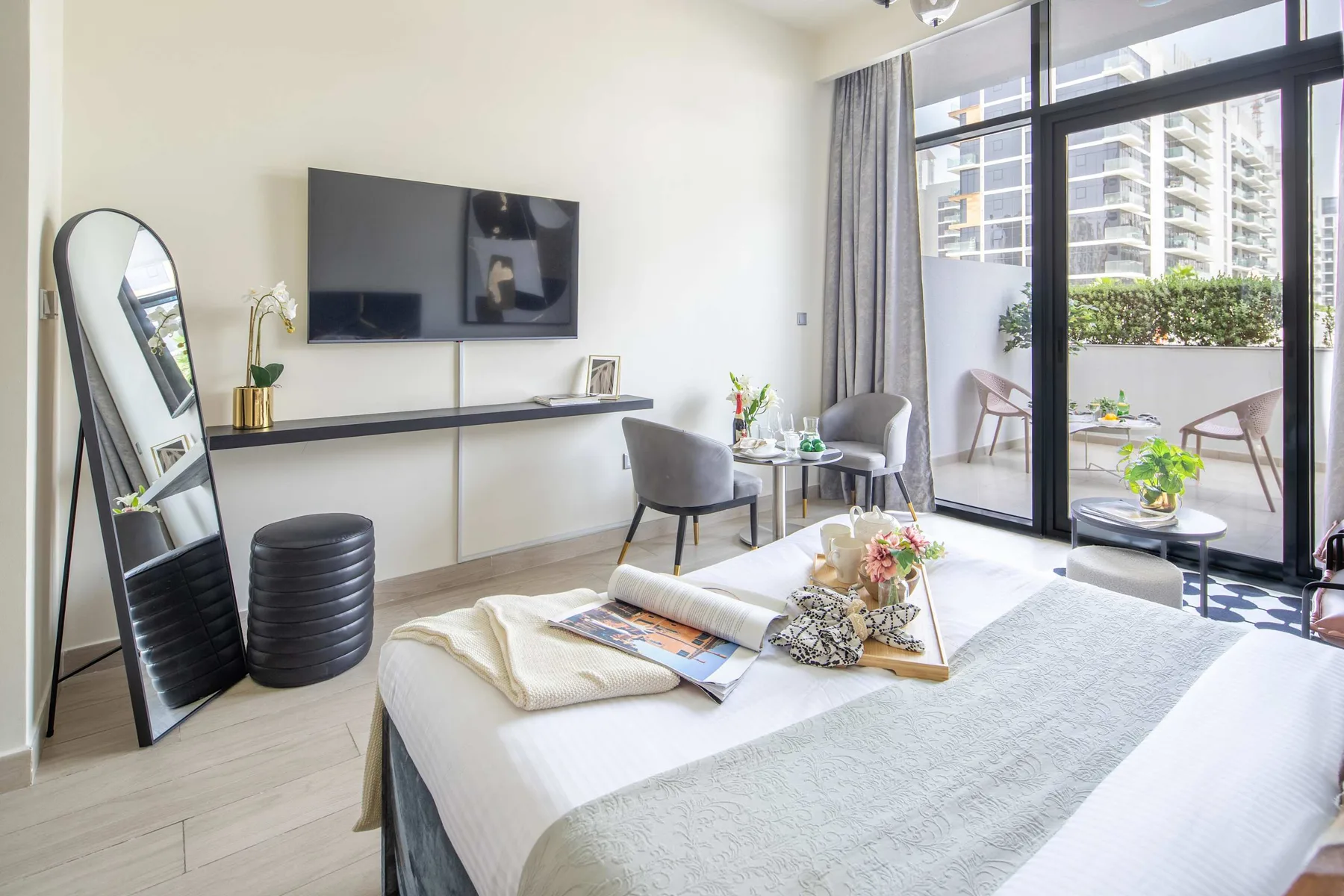Dormitorio luminoso con cama, zona de estar y puertas de vidrio hacia un balcón.