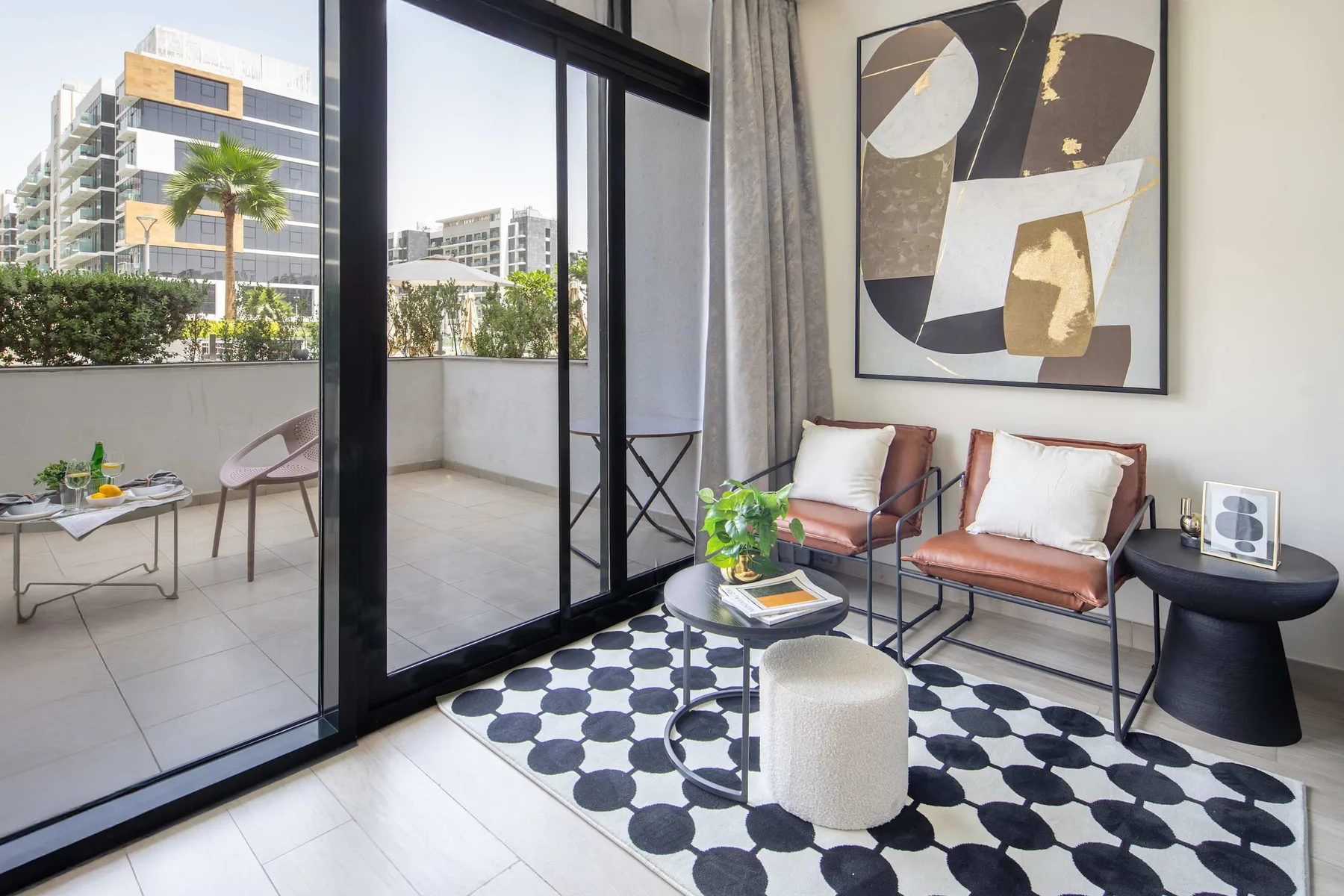 Una sala de estar moderna con asientos, una alfombra estampada y puertas de vidrio hacia un balcón.