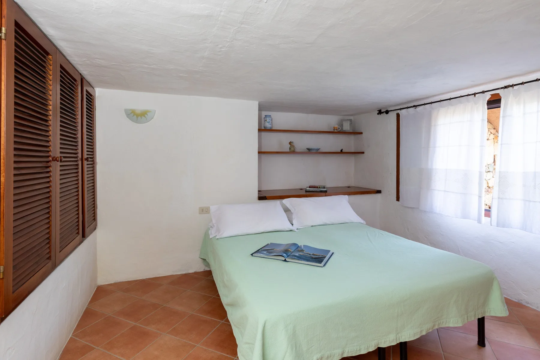 Un dormitorio con una cama cubierta con ropa de cama verde claro y estantes en la pared.