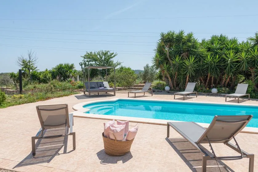 An outdoor swimming pool is surrounded by lounge chairs and greenery.