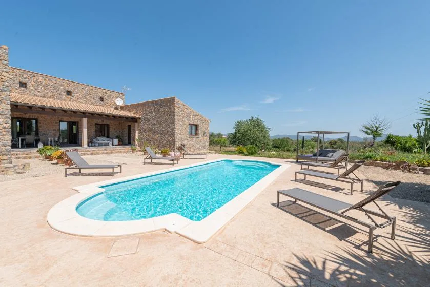 A swimming pool with lounge seating beside a stone building under a clear sky.