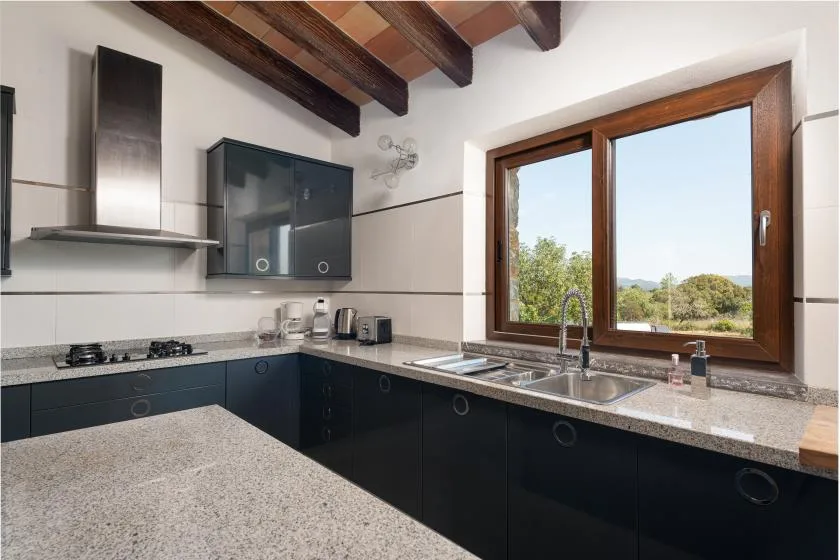 A modern kitchen with dark cabinets, a countertop, and a large window.