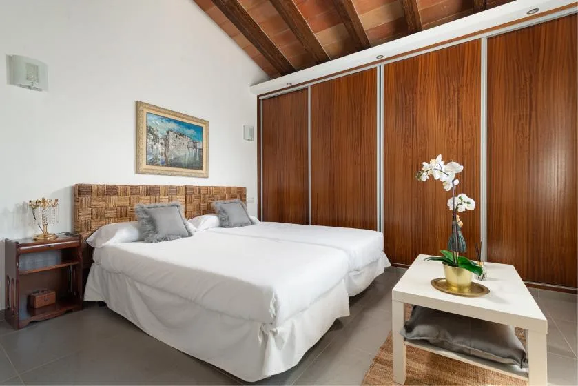 A bedroom with two beds, wood-paneled walls, and a small table holding an orchid.