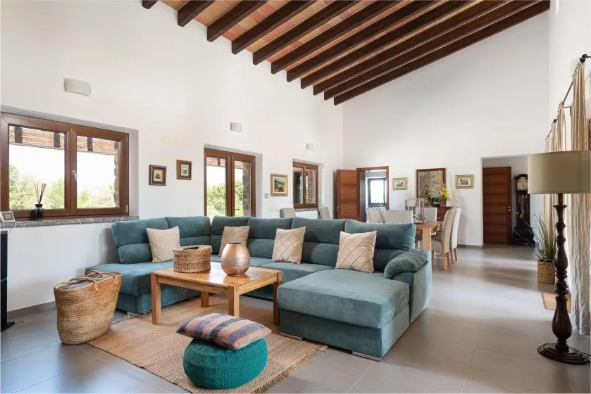 A bright living room with teal seating, a wooden coffee table, and exposed ceiling beams.