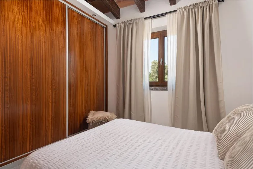 A bedroom with a bed, wooden wardrobe, and curtained window.